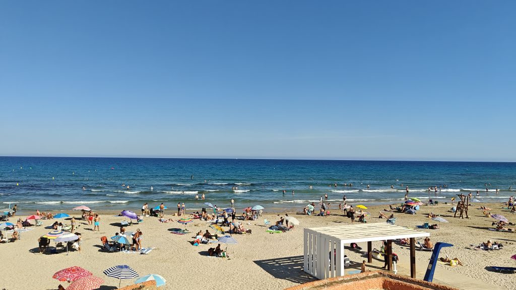 Blue sea and breaking waves beyond the parasols and a white beach shelter at La Zenia beach
