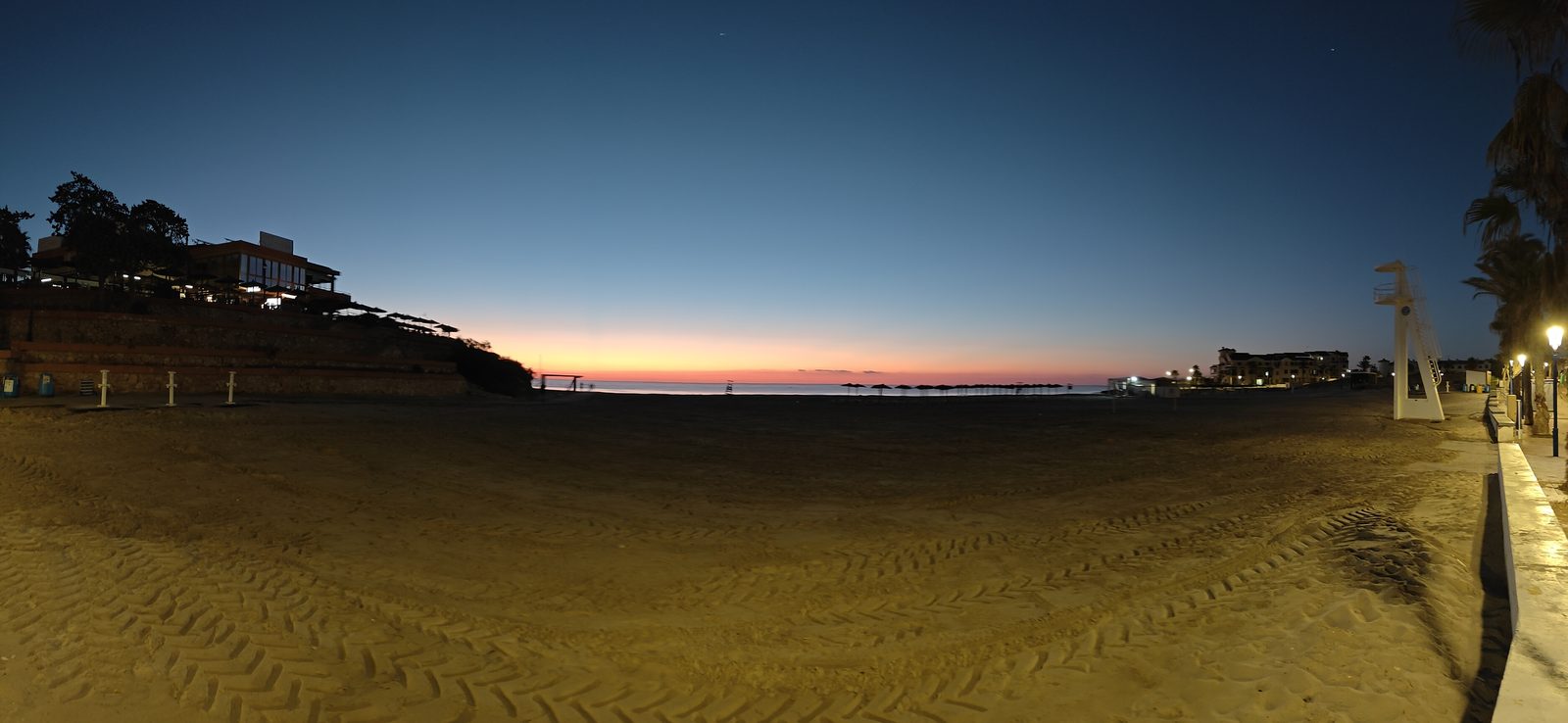 Wide view of La Zenia beach before sunrise, with the headland, a lifeguard chair and the promenade lights