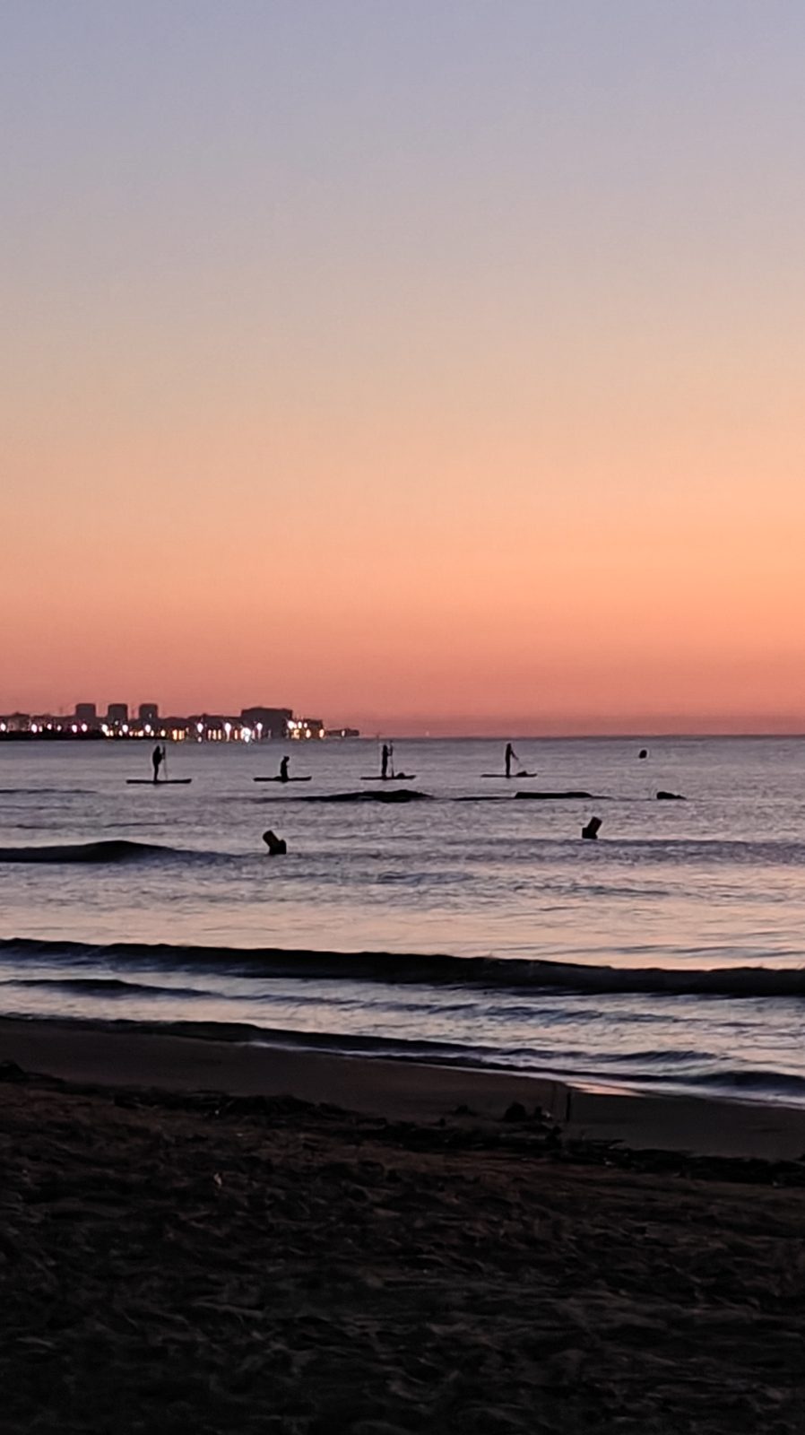 People out on a calm sea under a pink dawn sky off La Zenia beach