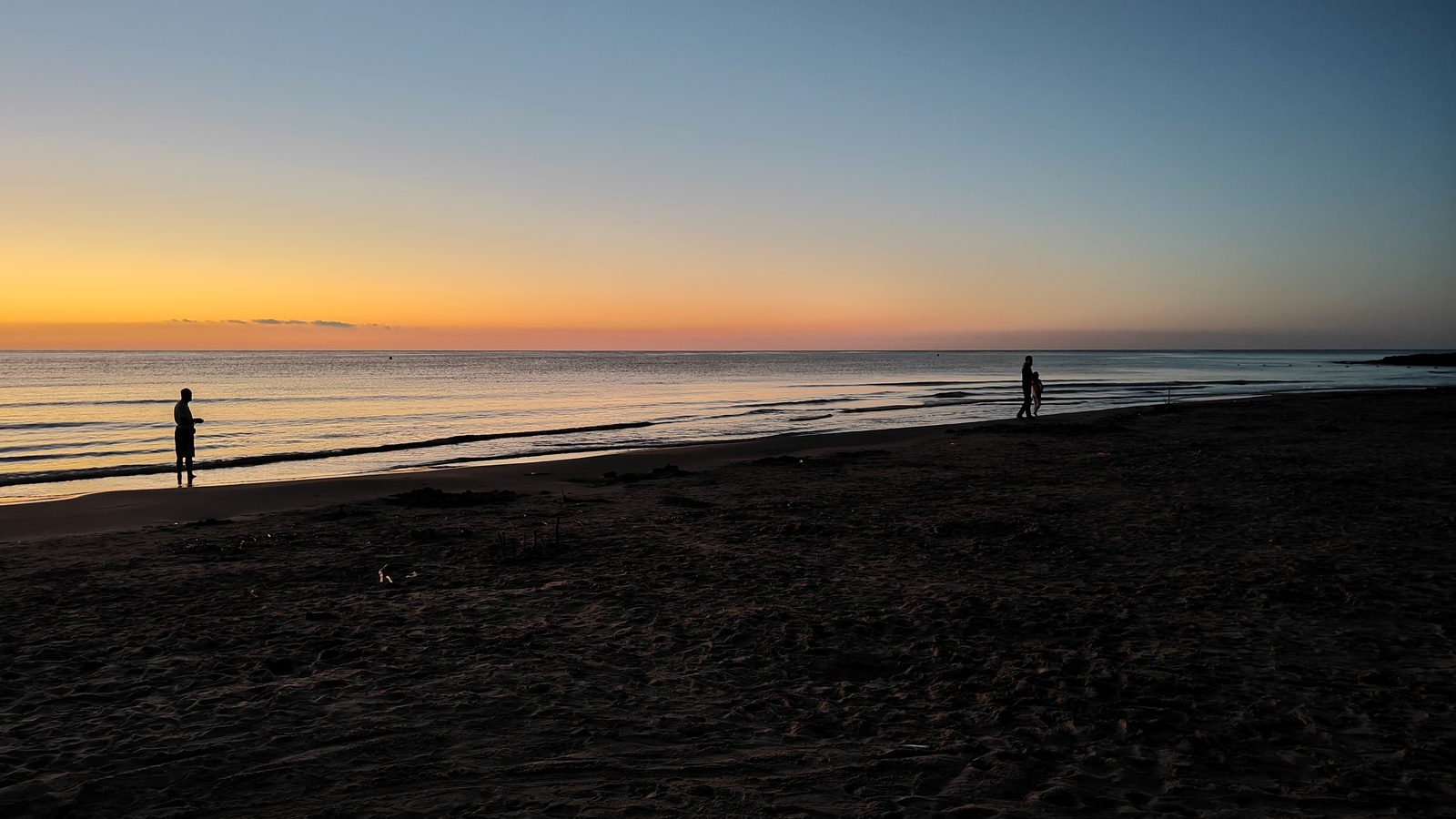Early-morning walkers silhouetted at the water's edge on La Zenia beach