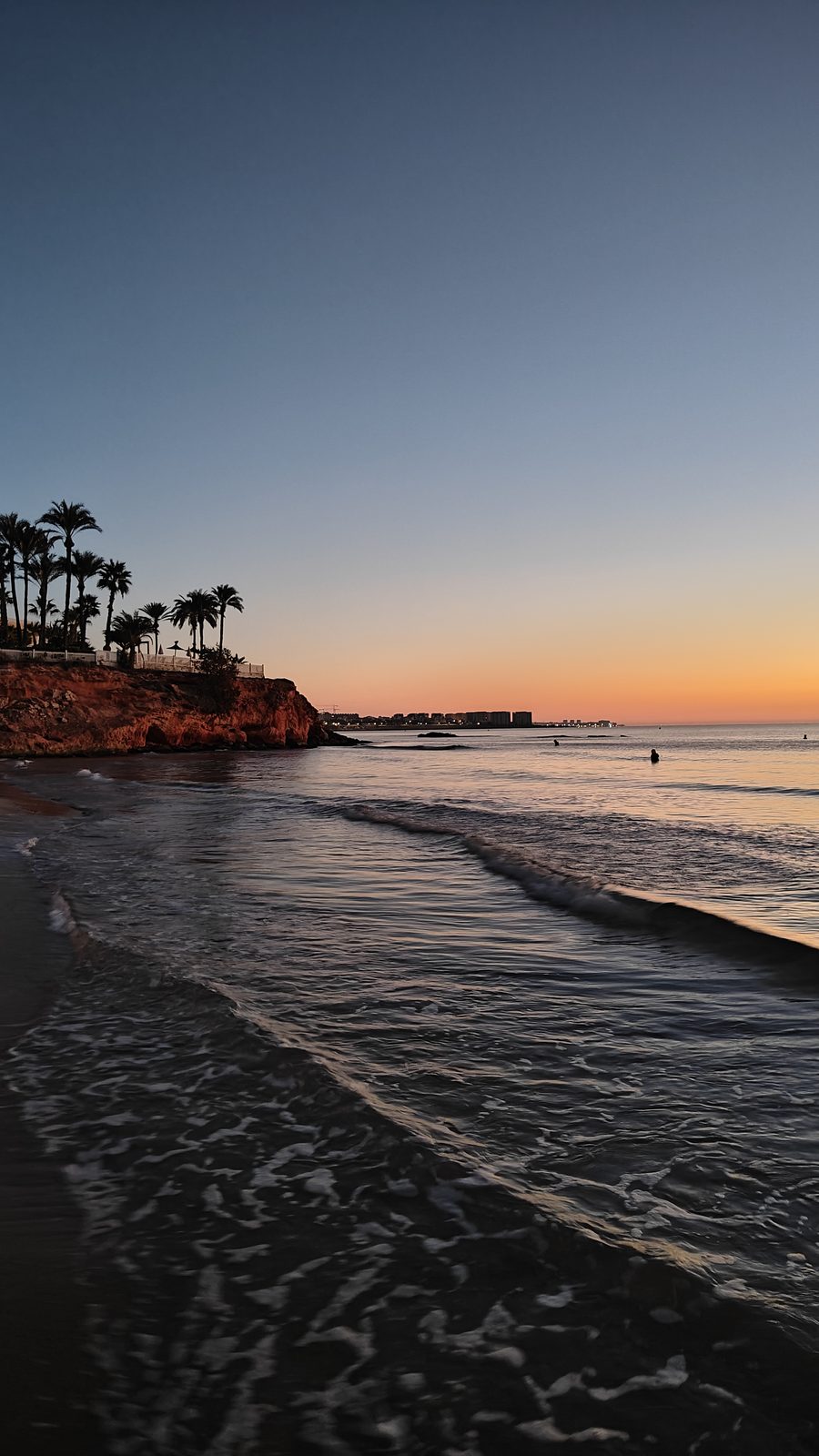 Palm-topped headland and gentle waves at La Zenia beach before sunrise