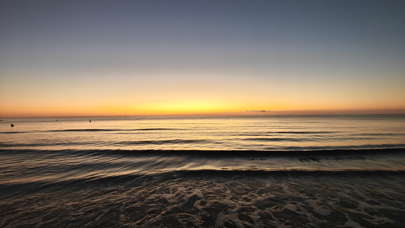 Golden light on the horizon over small waves at La Zenia beach at dawn