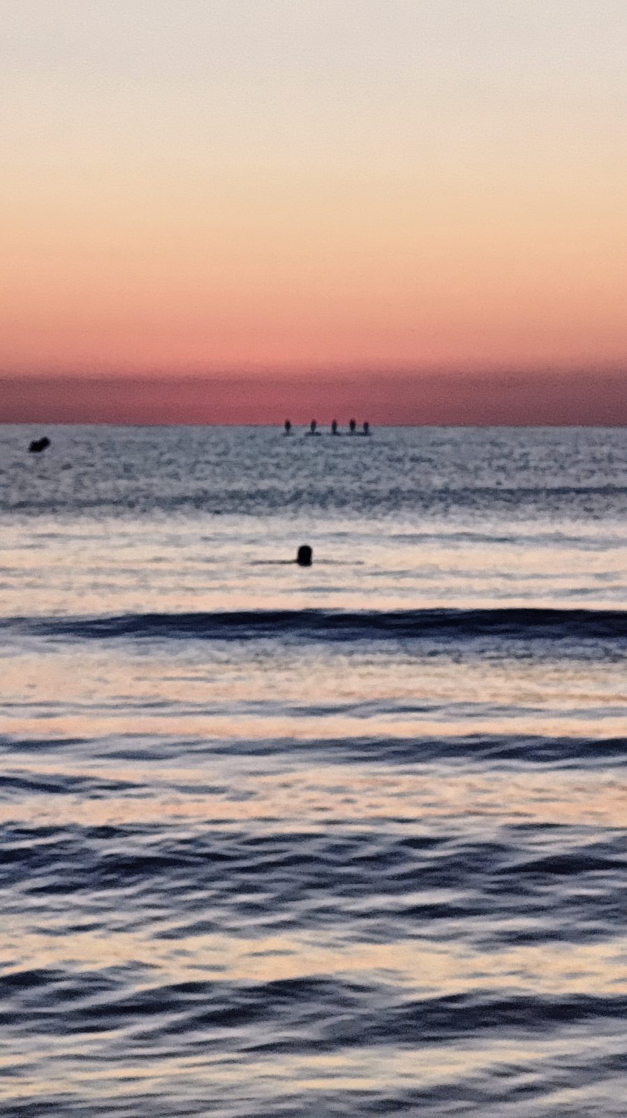 Figures on the water against a red band of dawn cloud off La Zenia beach
