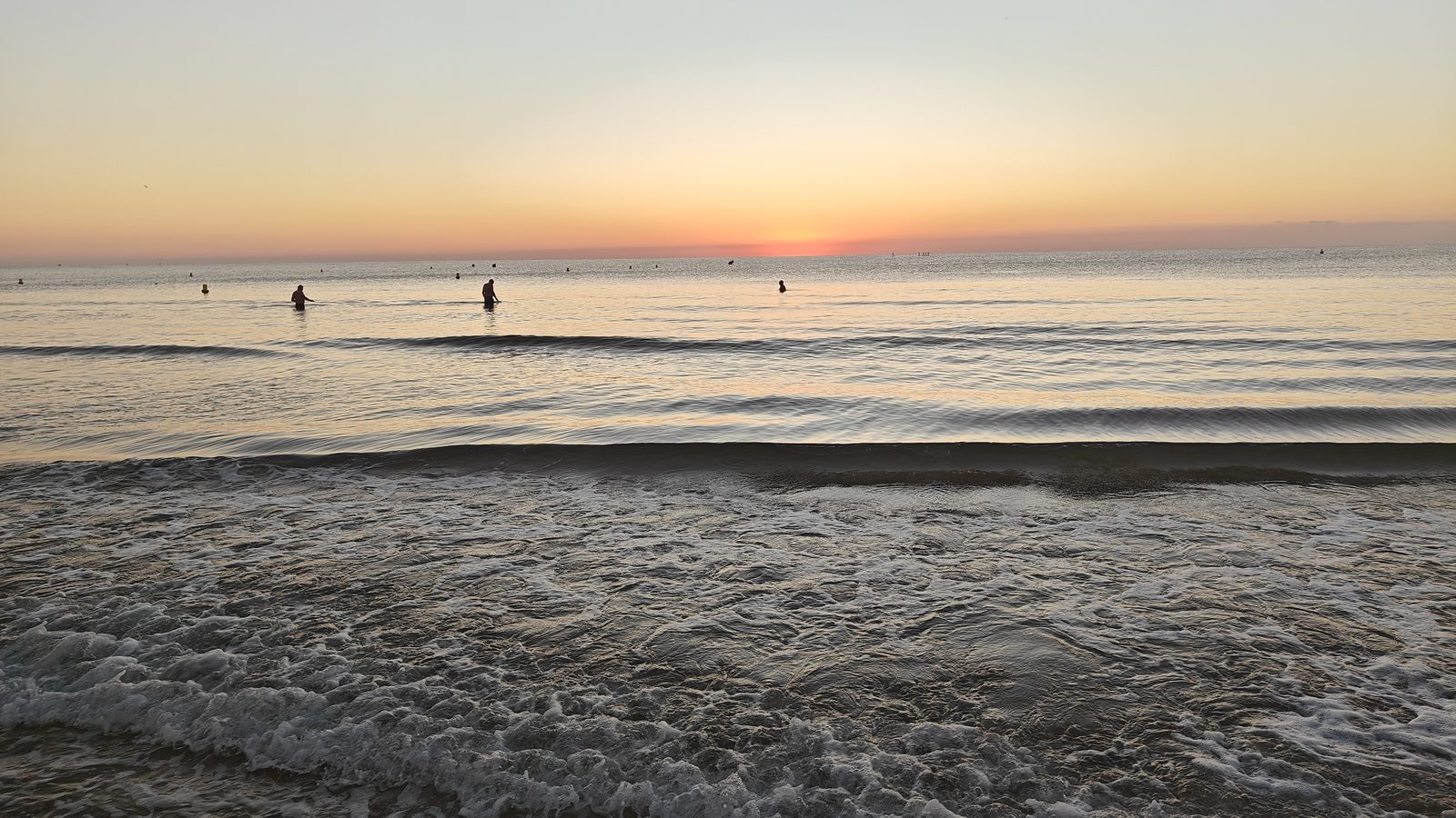 Swimmers standing in the shallows as the sun rises over La Zenia beach