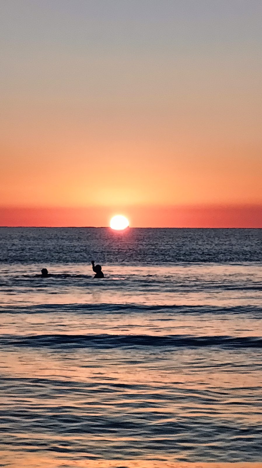 The rising sun above a red horizon, with a swimmer in the foreground at La Zenia beach