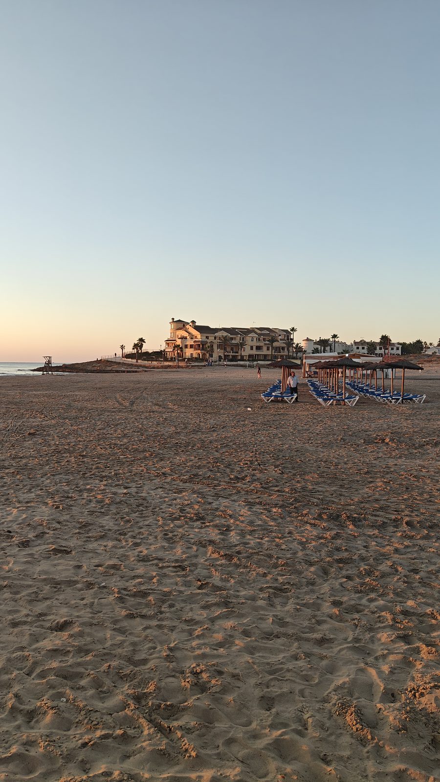 Sunbeds, straw parasols and seafront buildings in early-morning light at La Zenia beach