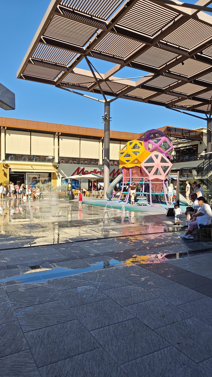 Ground-level water fountains and a colourful sculpture in a Zenia Boulevard plaza