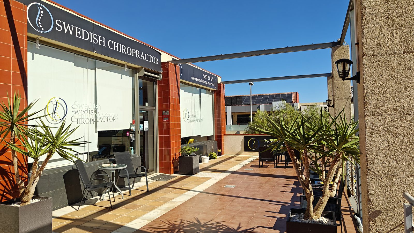 Shaded walkway past shopfronts and a clinic in Los Dolses